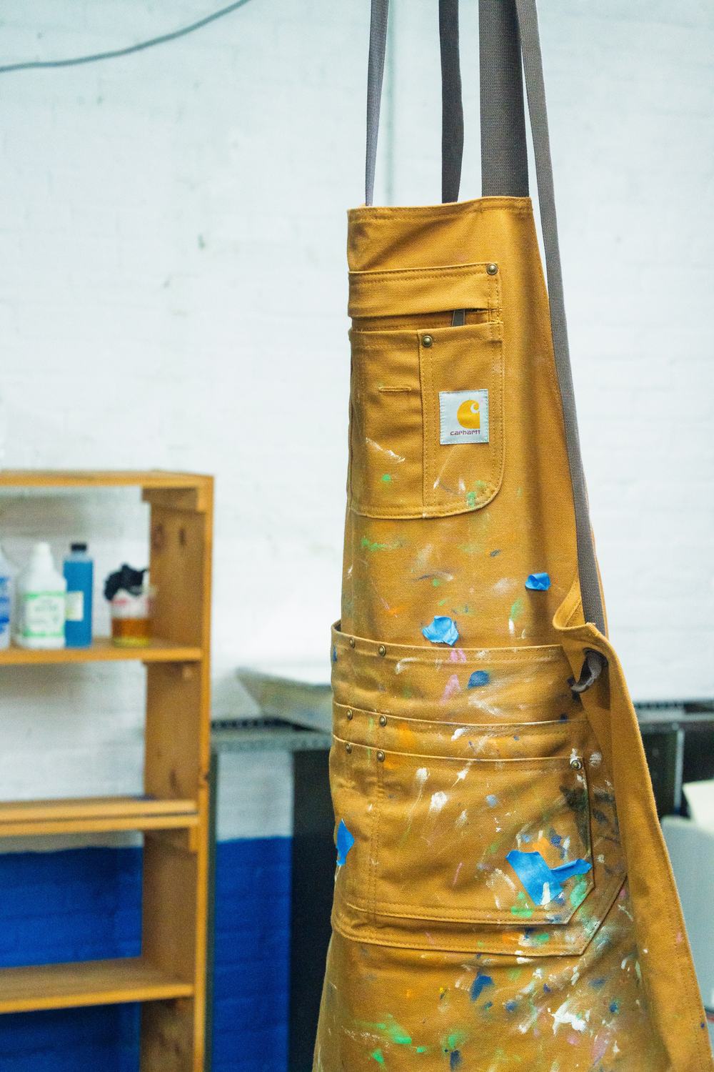 Close view of the printing apron: ink-stained pockets and tool loops against a whitewashed brick wall.