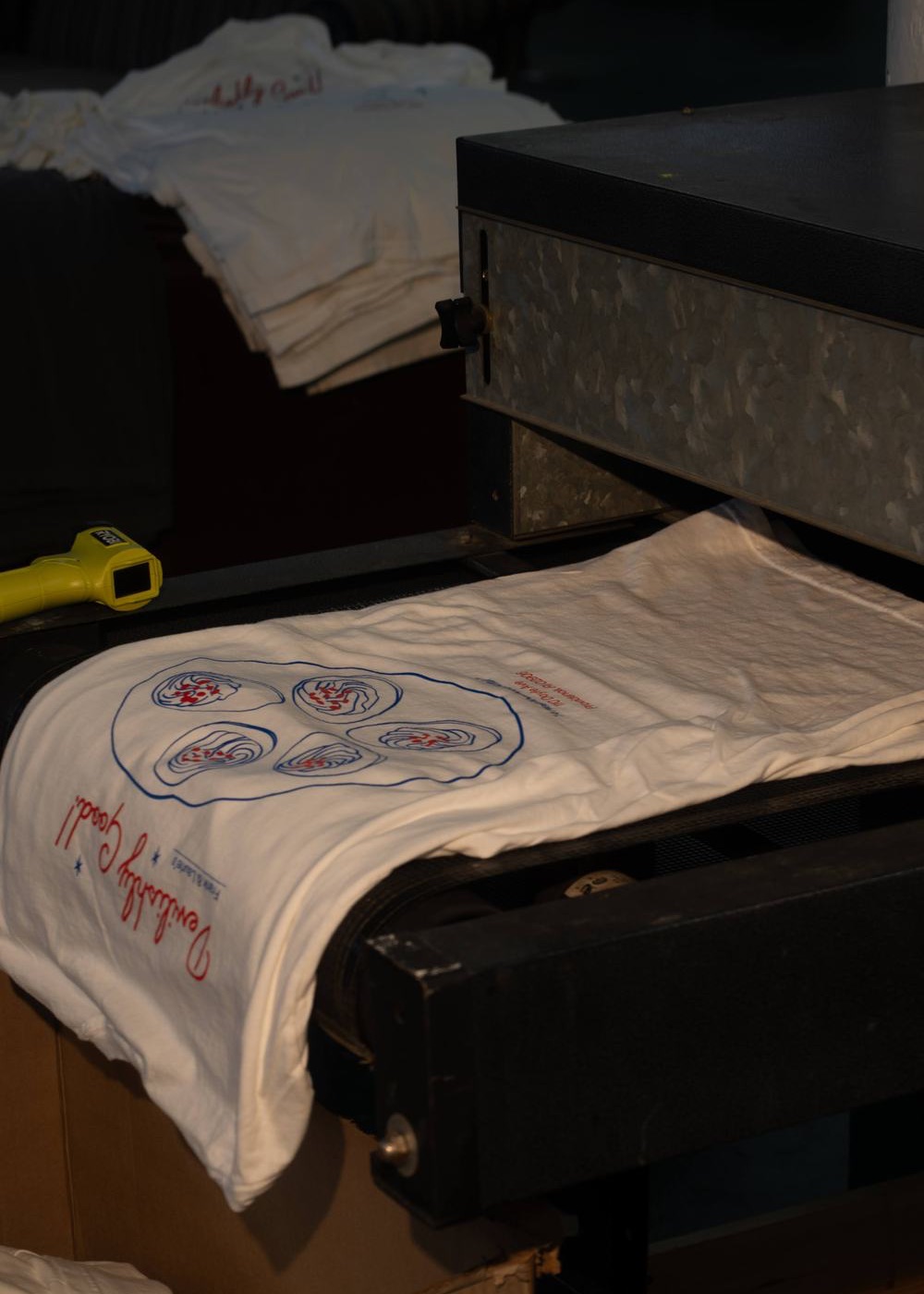 A printed shirt coming off the belt of the conveyor dryer, with an infrared temperature gun beside it.