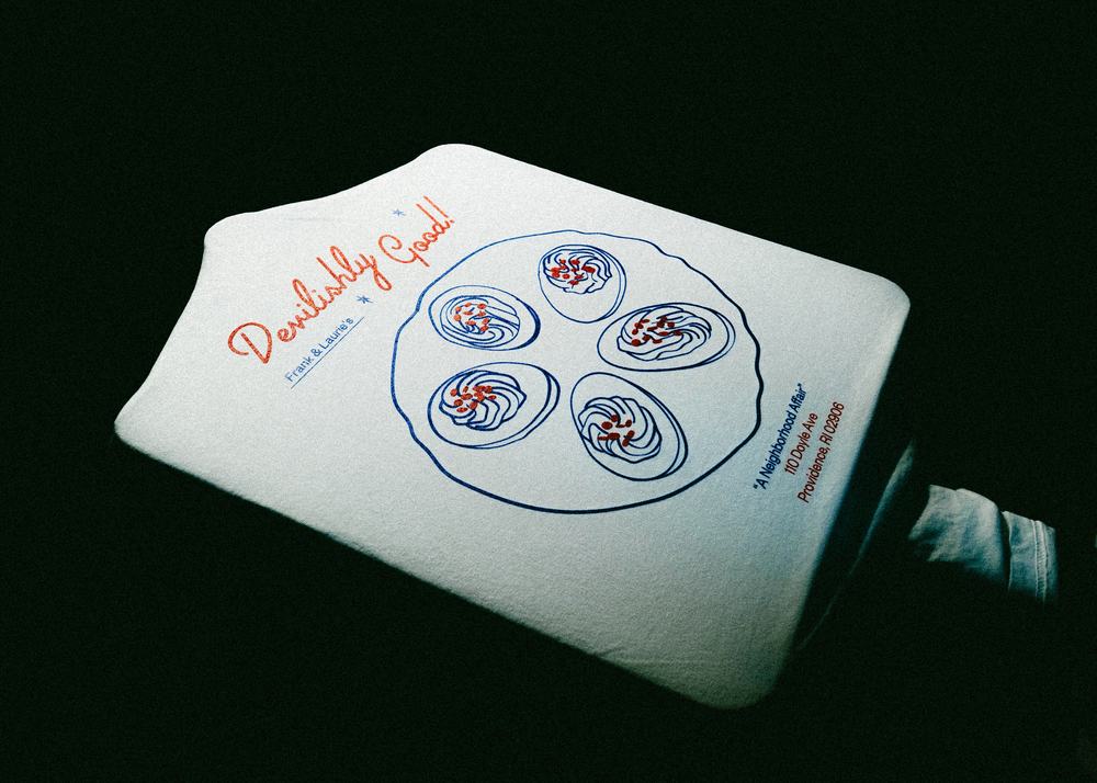 The finished Frank & Laurie’s shirt: hand-drawn oysters in blue with red accents and Devilishly Good! in script.