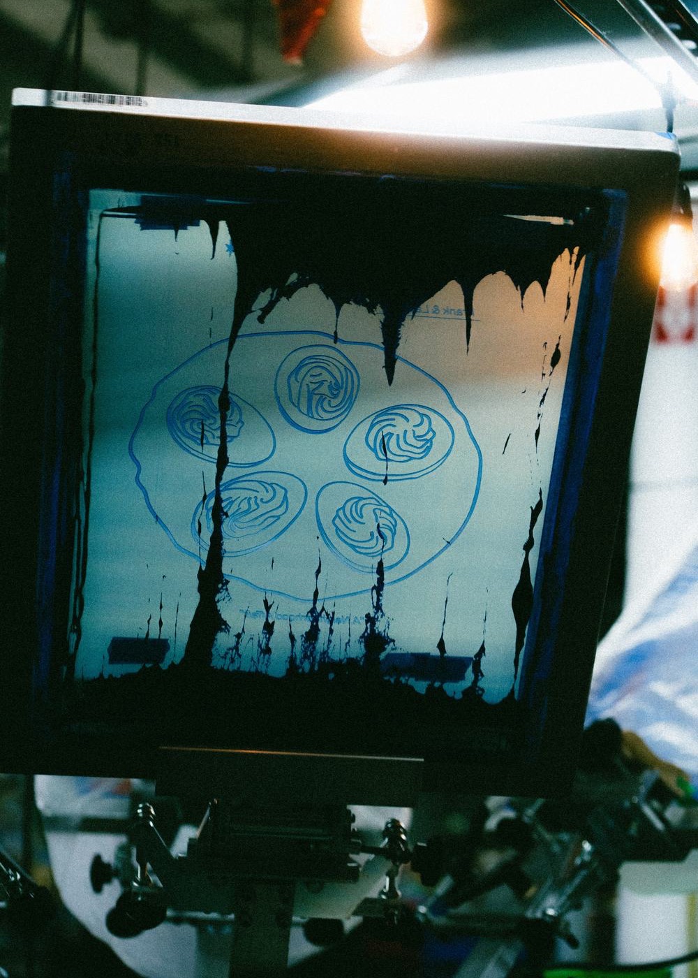 A coated screen on the press with the blue plate of the Frank & Laurie’s oyster illustration burned into the emulsion, ink flooded across the top.