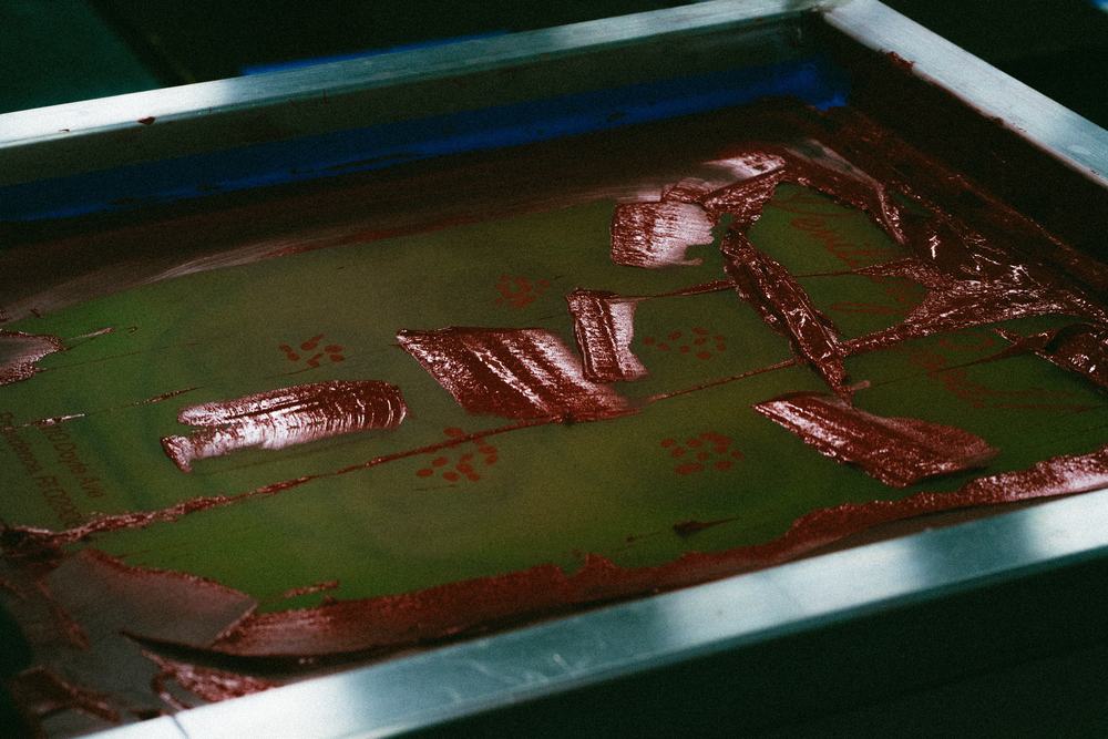 Red plastisol ink worked across a screen, the second color of a two-color job before the pull.